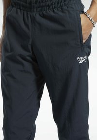 Schwarze Reebok-Jogginghosen mit elastischem Bund, Seitentaschen, glatter Textur und einem Logo am linken Oberschenkel. Lässige Passform für Komfort.