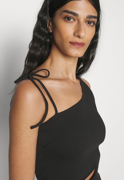 Débardeur asymétrique noir avec une découpe, doté d'un tissu texturé et de fines bretelles en douceur. Comprend un détail de poche sur le côté.