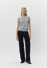 Pulover gri fără mâneci, cu guler rotund, asortat cu pantaloni largi de culoare albastră închisă, cu cusături contrastante. Textură de stofă netedă.