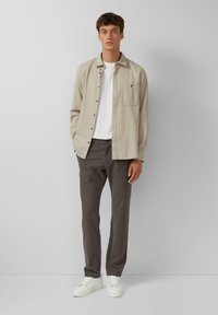 Beige overhemd met knopen boven een wit T-shirt, grijs met patroon broeken en witte sneakers. Eenvoudig ontwerp, lichtgewicht stof en neutrale kleuren.