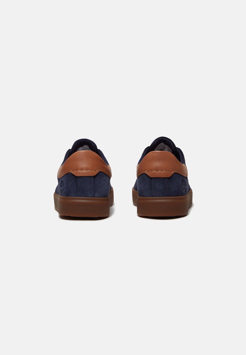 Scarpe in suede blu navy con dettagli in pelle marrone, un collare imbottito e suola in gomma. Presentano una punta arrotondata e un design minimalista.