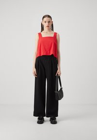 Red cropped tank top with a square neckline, paired with high-waisted black wide-leg trousers and chunky black shoes. Small black handbag.