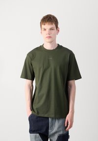 Olivegrünes Baumwoll-T-Shirt mit klassischem Rundhalsausschnitt, kurzen Ärmeln und einem dezenten Logo auf der Brust. Glatte Textur, entspannte Passform.
