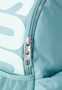 Šviesiai mėlyna kuprinė su tekstūruota paviršiumi, turinti iškilią užtrauktuką ir Nike logotipo etikete. Dizainas apima tinklinį kišenę.