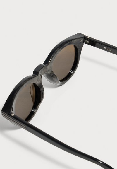 Lunettes de soleil en acétate noir avec verres ronds marron et marquage "ZEGNA" sur la branche, sur fond blanc.