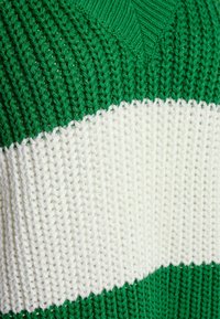 Sweter dziany z teksturowaną zieloną górną częścią i białym poziomym paskiem, prezentujący prążkowany wzór oraz dekolt w serek.