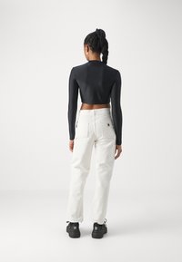 Top preto cropped de manga longa combinado com calças cargo brancas com bolsos laterais e ténis pretos com detalhes brancos no logo.