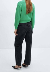 Zwarte high-waisted jeans met rechte pijpen, gecombineerd met een groene gebreide trui en zwarte hielmuilen, gezien vanaf de achterkant.