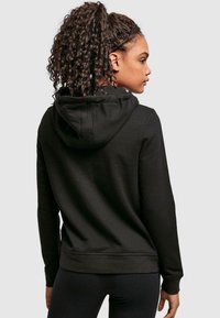 Sweat à capuche noir avec un tissu texturé, coupe décontractée et poche kangourou. La vue arrière met en avant un design doux et décontracté.