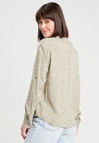 Long-sleeve shirt in light olive green fabric with a geometric pattern, buttoned cuffs, and a back pleat for added movement.