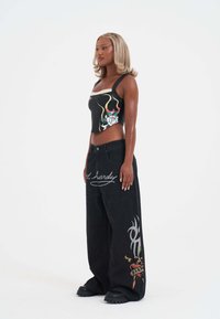 Top negro corto con gráficos florales y abstractos, combinado con jeans negros de corte holgado que presentan diseños bordados y detalles metálicos en plata.