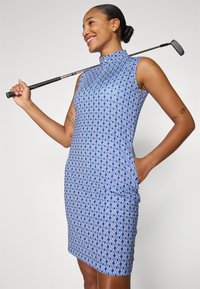 Modrá golfová šaty so vzorom, s vysokým golierom, bez rukávov a dvoma bočnými vreckami. Tkanina má geometrický vzor a hladkú štruktúru.