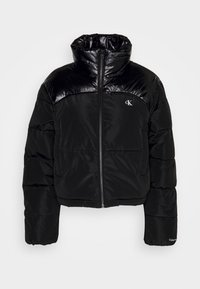 Giacca a vento nera con parte superiore lucida, chiusura con zip, colletto alto e polsini elastici. Presenta un piccolo logo sul lato sinistro del petto.