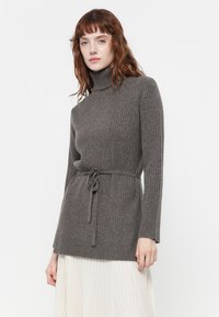 Siv turtleneck pulover z rebrastim vzorcem, ki ima pas in dolge rokave ter mehak texture, v kombinaciji s kremasto plisirano krilo.