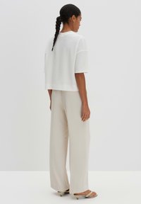 Witte gebreide crop top met korte mouwen, gecombineerd met beige wijde broekspijpen. Model staat met de rug naar de camera, toont de relaxte pasvorm van de outfit.