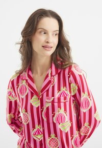 Camisa de pijama a rayas rosas y rojas con estampados de adornos coloridos, un bolsillo en el pecho y un diseño de cuello clásico. Textura de tela suave.