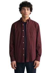 Camisa burdeos de botones con cuello, hecha de tejido texturizado. Presenta un bolsillo de parche y botones blancos, superpuesta sobre una camisa azul marino.