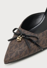 Chaussure marron à bout pointu avec motif, nœud noir et petit pendentif doré à l'avant, avec une doublure intérieure noire lisse.