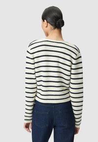 Maglione a righe con lavorazione a maglia testurizzata in crema e navy, con scollatura ampia, maniche lunghe e silhouette cropped abbinato a jeans scuri.