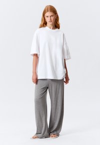White oversized cotton t-shirt paired with gray wide-leg knit pants; model stands barefoot, displaying relaxed fit and soft texture.