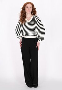 Maglione a righe bianco e nero con scollo a V e maniche a sbuffo, abbinato a pantaloni neri a gamba larga e scarpe nere semplici.