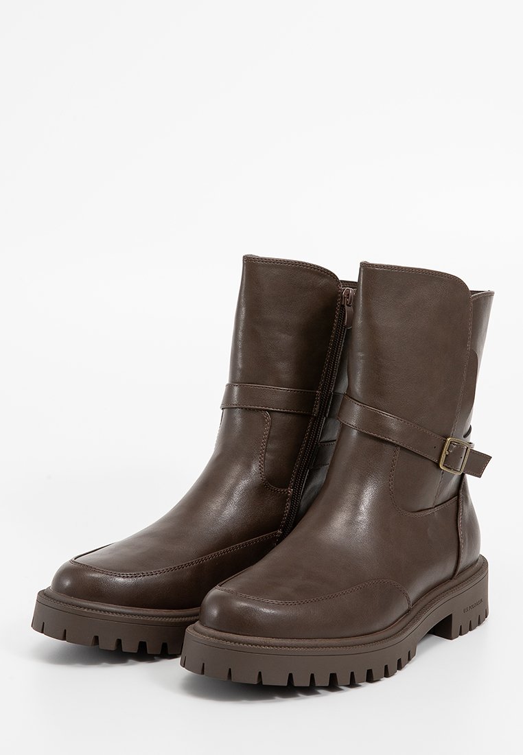 Bottes chevilles en cuir marron avec une fermeture éclair sur le côté, une sangle réglable avec une boucle, une semelle en caoutchouc épaisse et une finition texturée.