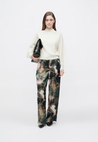 Hvid tekstureret sweater med lange ærmer, kombineret med løstsiddende bukser med blomsterprint i mørkegrøn og creme. Sort clutch taske.