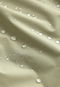 Gouttelettes d'eau perlent sur un tissu imperméable lisse de couleur beige clair avec de légers plis et une texture douce visible.