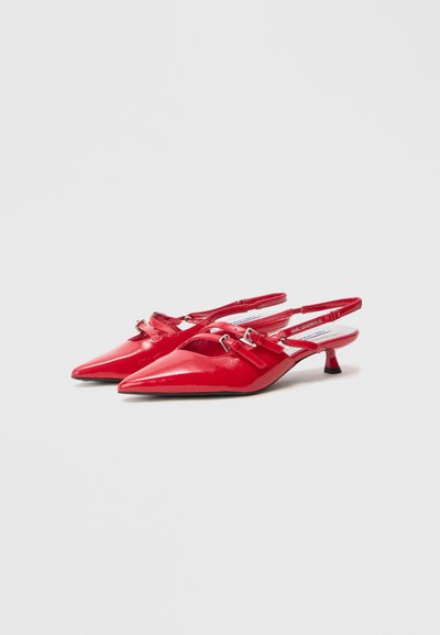 Red patent leather slingback heels with a pointed toe, featuring a buckle detail and a small kitten heel. Smooth texture and shiny finish.