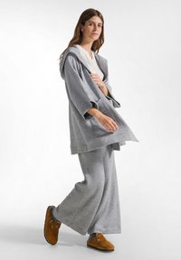 Grijze, hooded, overgrote cardigan met wijde mouwen, gecombineerd met bijpassende grijze wijde broek. Bruine instappers met banden maken de outfit compleet.