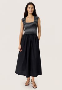 Musthave, pahklaiiseline must kleit, millel on selga istuv triibuline kehaosa ja laienev seelik. Omab ruudukujulist kaelust ja küljetaskuid. Minimalistlik disain.