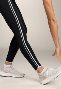 Black leggings with white side stripes, featuring a smooth texture. Pair of light-colored athletic shoes with mesh and rubber accents.