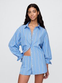 Blåstripet skjorte med knapper og overdimensjonerte ermer, knyttet i livet, sammen med matchende shorts. Stoffet ser glatt og lett ut.