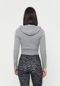 Gray cropped hoodie with a hood, ribbed hem, and long sleeves. Paired with black leggings featuring a contrasting zebra print pattern.