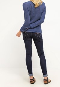 Blauer Strickpullover mit langen Ärmeln, kombiniert mit dunklen Skinny-Jeans, die am Saum aufgerollt sind, und braunen Plateausandalen.