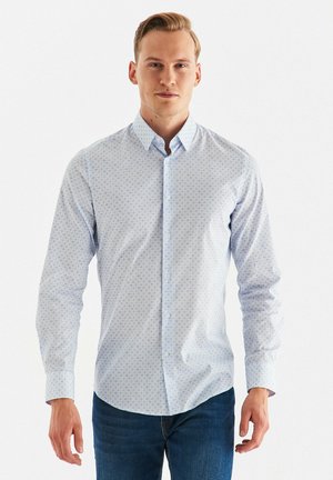 Jasnoniebieska koszula z długim rękawem, z subtelnym wzorem i rozłożystym kołnierzykiem. Tekstura materiału wydaje się gładka i lekka.