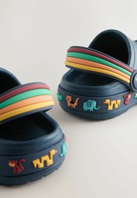 Zoccoli in gomma blu navy con cinturini multicolori flessibili e decorazioni a forma di animali sul lato. Design con apertura sul retro per un facile utilizzo.