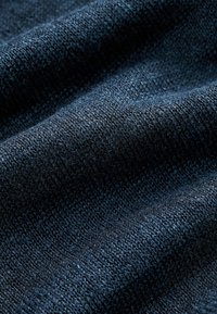 Gros plan sur un tissu tricoté bleu foncé montrant une texture détaillée et un motif tissé avec des plis doux.