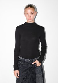 Musta pitkähihaisia paita, jossa on korkea kaulus. Valmistettu sileästä ja joustavasta materiaaleista. Yhdistetty harmaisiin farkkuihin, joissa on teksturoitu vyötärö.