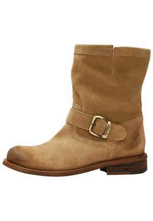 Tan suède enkellaars met een brede band en een metalen gesp, en een structuurzool. Ronde neus en een lichte hak met een eenvoudige logo-detail.