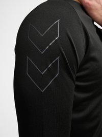 Gros plan sur la manche d’une chemise noire à manches longues avec deux bandes gris foncé en forme de chevron sur le haut du bras.
