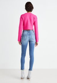 Feszes, élénk rózsaszín bordás crop pulóver világoskék, magas derekú skinny farmernadrággal párosítva. A modell ezüst színű, csipkés szegélyű bokacsizmát visel.