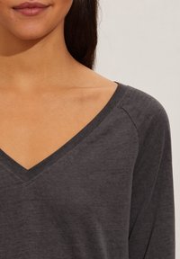 Grå V-ringad topp med långa ärmar, tillverkad av mjukt tyg. Har en avslappnad passform och minimal sömnad längs halsringningen och axlarna.