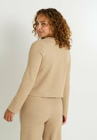 Chaqueta recortada texturada beige de manga larga, con un cuello redondo y pantalones a medida a juego, vista desde la parte de atrás.