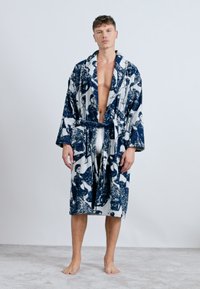 Modrá a biela vzorovaná toaleta s opaskom, vyrobená z mäkkej tkaniny. Má golier v štýle kimono a dlhé rukávy.