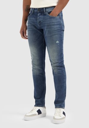 Dark blue denim jeans with a slim fit, featuring fading, whiskering details, and subtle distressing near the pockets. Classic five-pocket design.