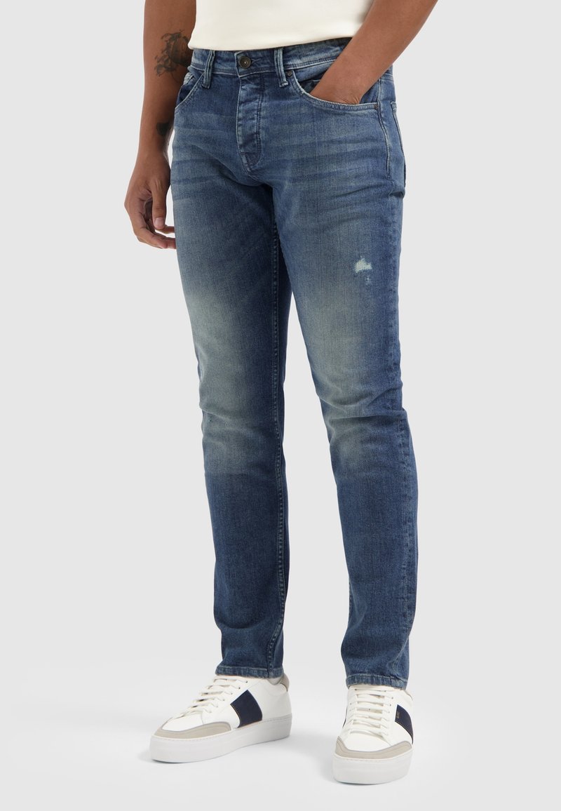 Donkerblauwe denim jeans met een slim fit, voorzien van vervaging, whiskering details en subtiele slijtage nabij de zakken. Klassiek vijf-pocket ontwerp.
