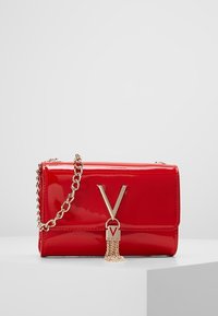 Borsa a mano in pelle verniciata rossa con una tracolla in catena dorata, caratterizzata da un'emblema a forma di V e un dettaglio a frange. Forma rettangolare compatta.