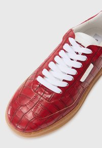 Baskets en cuir rouge gaufré crocodile avec des lacets blancs, bouts ronds et semelle en caoutchouc beige. Présente un logo discret sur le côté.
