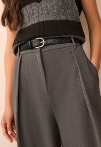 Sweter z mieszanki wełny z szaro-czarnymi paskami, zestawiony z szarymi spodniami z wysokim stanem oraz czarnym paskiem o fakturze z srebrną klamrą.